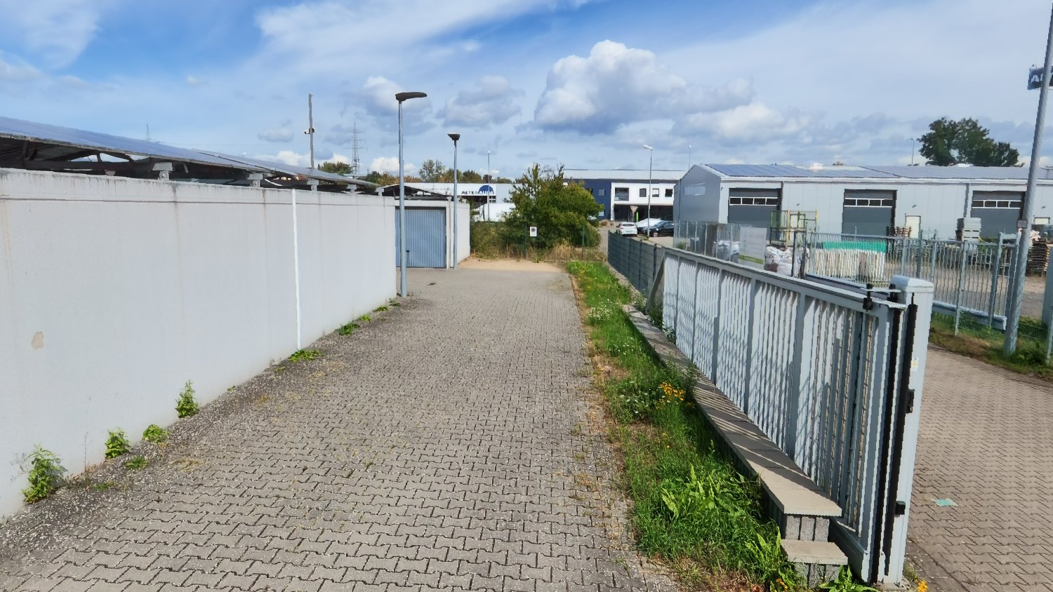 Einfahrt mit elektrischem Schiebetor und Zaun, dahinter das Gewerbegebiet Im Hundel